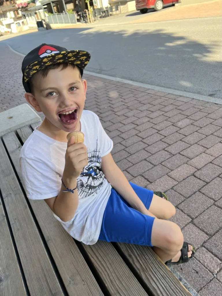 Strahlender Bub mit Eiswaffel auf einer Bank in Neukirchen